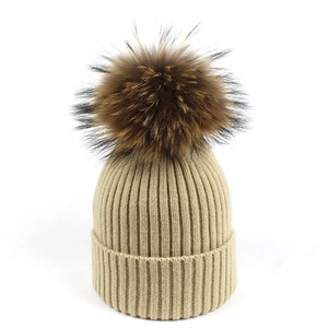 Detalle de gorro de punto acanalado beige con un gran pompón de piel natural elegante
