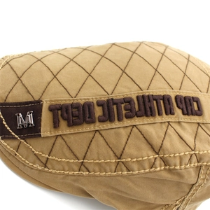 Macro detail of khaki quilted canvas hat featuring brown athletic embroidery and silver M badge
