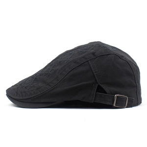 Close-up of black canvas flat top beret featuring geometric embroidery and metal buckle