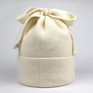 Close-up of cream ribbed knit winter hat featuring a large decorative bow detail