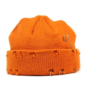 Macro detail of orange knit beanie with metal safety pin and rings on distressed brim