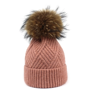 Detail of dusty pink knit beanie with ribbed texture and fluffy raccoon fur pom pom
