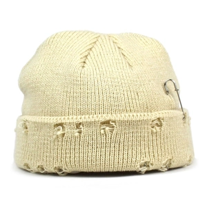 Detail of off-white knitted beanie featuring distressed holes and silver safety pin accessory