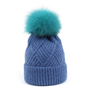 Detail of navy knit beanie texture with a fluffy teal faux fur pom pom on top