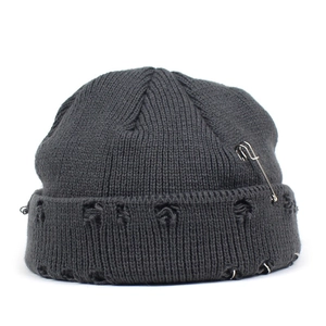 Detail of grey distressed knit beanie featuring silver safety pin and metal ring accents