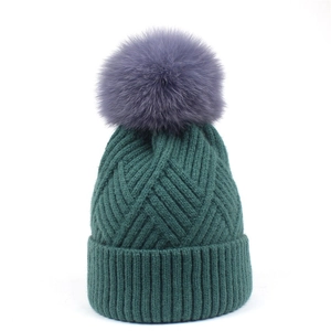 Detail of dark green knit beanie featuring ribbed texture and large grey faux fur pom-pom