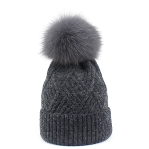 Warm dark grey knitted winter beanie for women featuring a large fluffy faux fur pompom