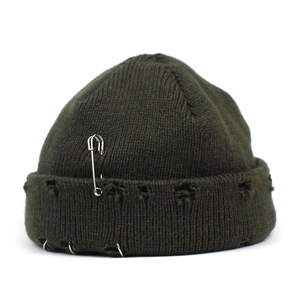 Detail of distressed olive green knit beanie with safety pin and metal rings decor