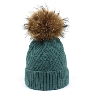 Detailed knit texture of dark green winter beanie featuring a fluffy brown fur pompom