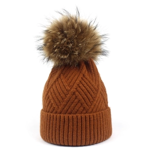 Detail showing caramel knitted beanie with diamond texture and large fluffy pompom