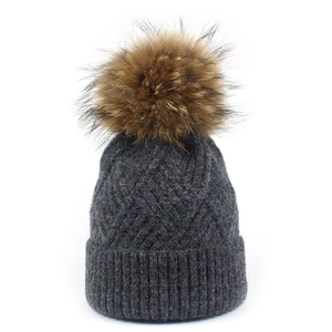 Close-up of dark grey cable knit beanie with fluffy faux fur pompom and ribbed cuff