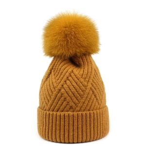 Close-up of mustard yellow knit hat with fluffy faux fur pompom and ribbed cuff detail