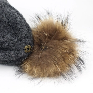 Detail of dark grey knit hat showing soft fur pom-pom and vintage metal button