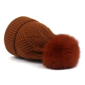 Detailed close-up of dark brown knit beanie with large fluffy faux fur pom-pom