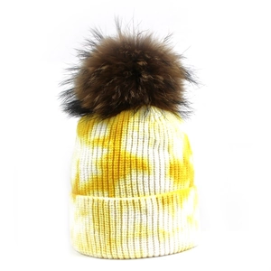 Détail du tricot tie-dye jaune montrant la texture et le pompon en fourrure du bonnet