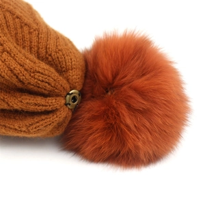 Detail of detachable fluffy fur pompom with metal snap button on orange knit beanie