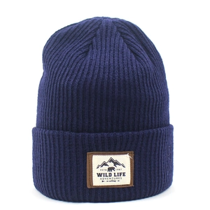 Detail of dark blue ribbed knit beanie featuring an outdoor mountain patch on the fold