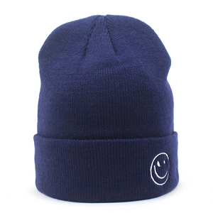 Dettaglio ravvicinato del berretto in maglia blu navy con logo smile bianco ricamato sul risvolto