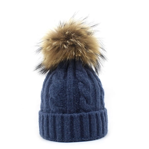 Close-up of cable knit texture and faux fur pompom on the navy blue wool beanie