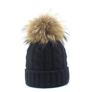 Close-up of black cable knit beanie with fluffy pompom detail and ribbed cuff