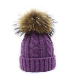 Detail of purple cable knit wool beanie featuring a plush faux fur pom-pom and ribbed cuff
