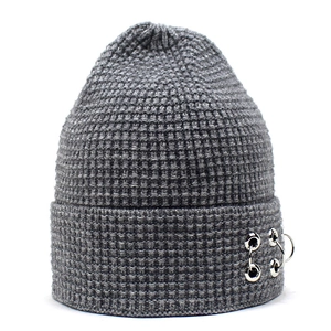 Détail d'un bonnet gris en maille gaufrée avec trois anneaux métalliques sur le rebord