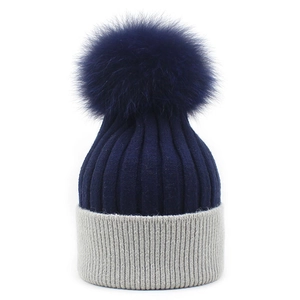 Detail of blue and grey knit beanie showing thick ribbed texture and large fluffy pompom