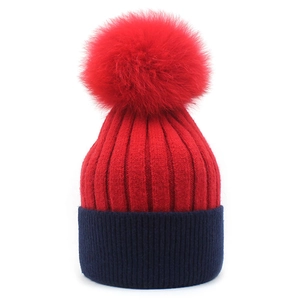 Detail view of contrast knit hat featuring red faux fur pom-pom and blue cuffed brim
