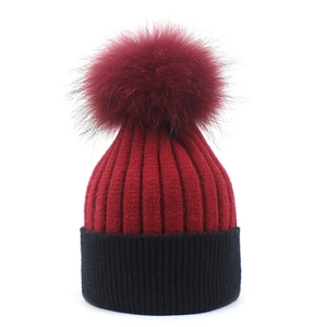 Detail of burgundy and black knit beanie with plush faux fur pompom and ribbed texture