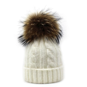 Close-up of white cable knit beanie with fluffy brown faux fur pom-pom detail