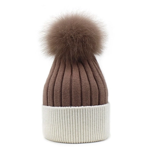 Detail of two-tone knit beanie featuring a large fluffy faux fur pompom on top