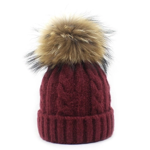 Detailed close-up of wine red cable knit beanie with premium faux fur pom-pom texture