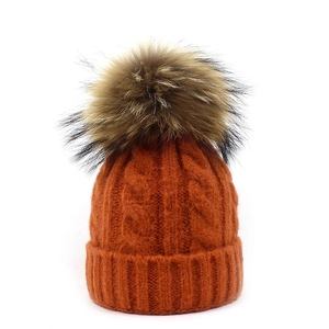 Close-up of orange cable knit beanie with fluffy pom-pom and thick ribbed cuff detail