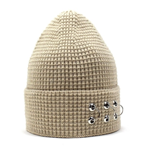 Détail du bonnet en maille beige avec anneaux métalliques décoratifs sur le revers