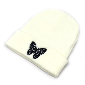 Close-up of fine black butterfly embroidery on off-white knitted beanie with folded edge