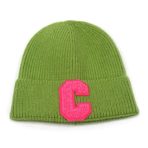 Dettaglio del berretto in maglia verde con toppa lettera C ricamata in spugna rosa