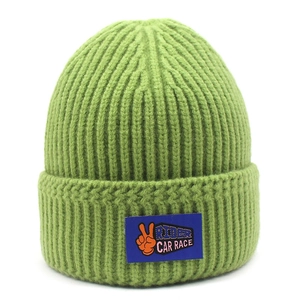 Detail of green ribbed knit beanie showing blue label with orange victory sign icon