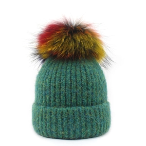 Detail einer türkisgrünen Strickmütze mit buntem Bommel auf weißem Hintergrund