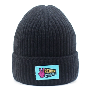 Detail of black ribbed knit beanie with blue RIDER logo patch and pink peace sign