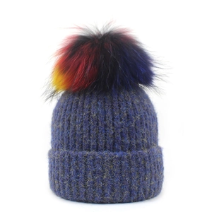 Detailansicht einer blauen Rippstrickmütze mit einem großen bunten Kunstpelz-Pompon