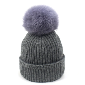 Detalle del gorro de punto gris oscuro con un gran pompón morado de pelo sintético