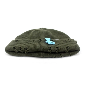 Detail of army green distressed knit beanie featuring a cute blue bear charm and torn edges