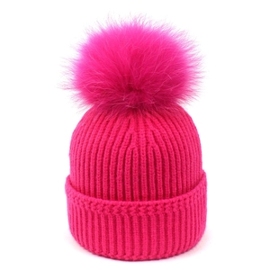 Detalle de gorro de punto rojo rosa con un gran pompón de piel de zorro real suave
