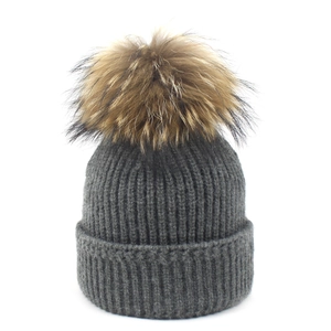 Detail of dark grey ribbed knit beanie featuring a fluffy real raccoon fur pom-pom topper