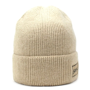 Dettaglio ravvicinato di un berretto in maglia a coste beige con toppa logo ADER