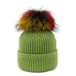 Detailed view of green ribbed knit beanie featuring a colorful fluffy raccoon fur pompom