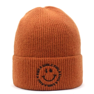 Close-up of ginger yellow knit beanie featuring black smile embroidery and ribbed texture