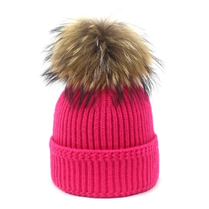 Close-up of ribbed knit rose red beanie with a fluffy brown raccoon fur pompom detail