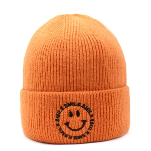 Close-up of orange knitted beanie featuring a black smile face and letter embroidery