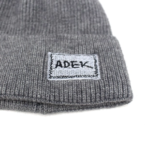 Berretto invernale in maglia a coste grigia con patch logo ADEK su sfondo bianco